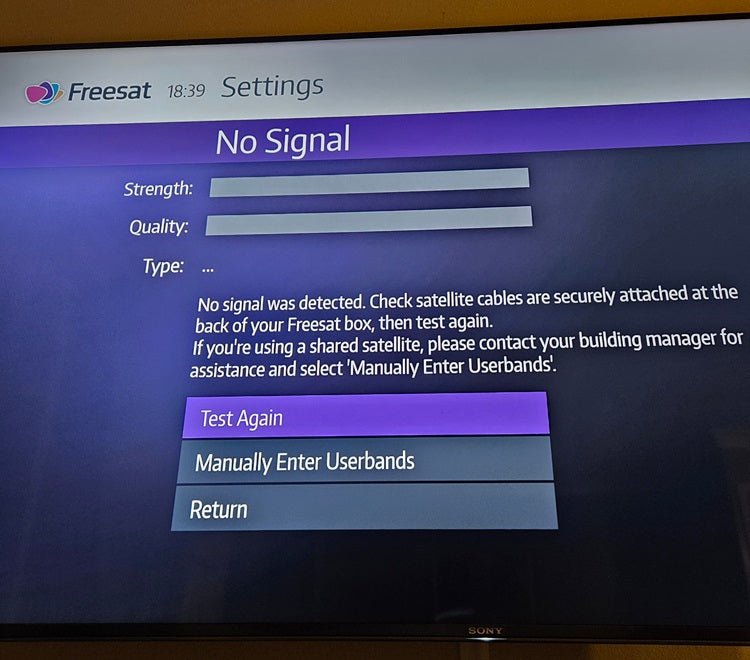Freesat box settings screen showing no signal error with options to test again, manually enter userbands, or return for satellite setup in shared buildings